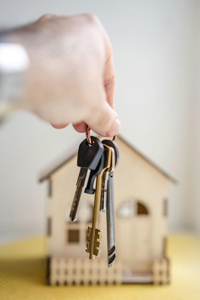 A hand holding keys over a wooden house.
